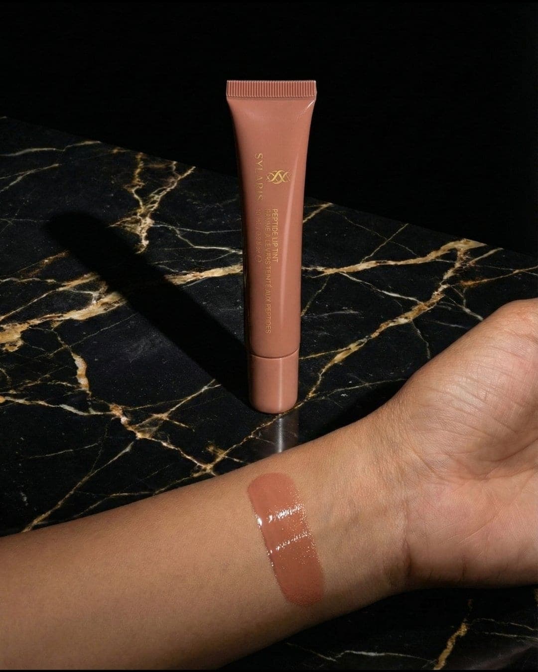 Nude Sylaris lip tint swatch on a wrist over black marble, AI-generated ad still