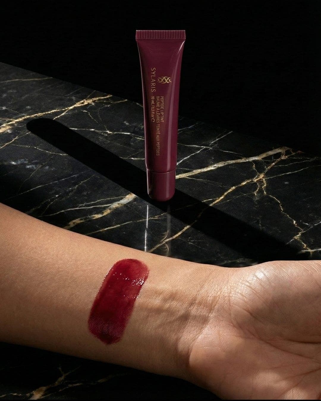 Berry Sylaris lip tint swatch on a wrist over black marble, AI-generated ad still